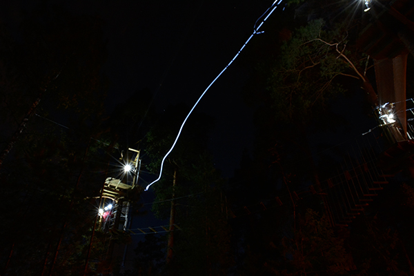 Tarzan swing at Treetop Adventure Huippu in the dark, lightpath of a headlamp in the air.