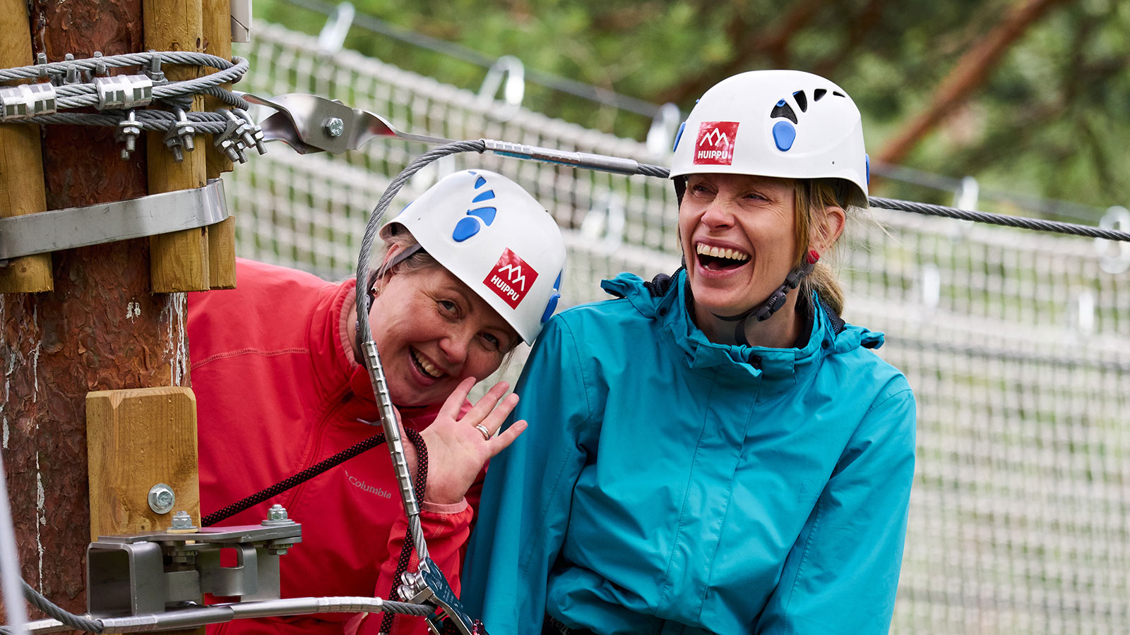 Kaksi naista nauraa makeasti Seikkailupuisto Huipun yläköysiradoilla.